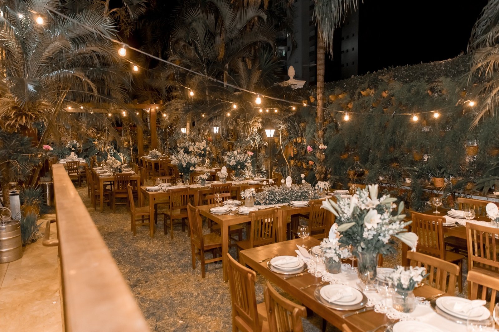 Jardim do Espaço Oz à noite com mesas postas e varal de luzes para festa de casamento