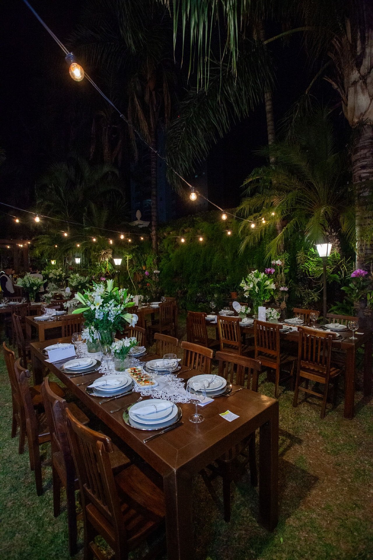 Jardim das Orquídeas do Espaço Oz à noite com varal de luzes e mesas postas
